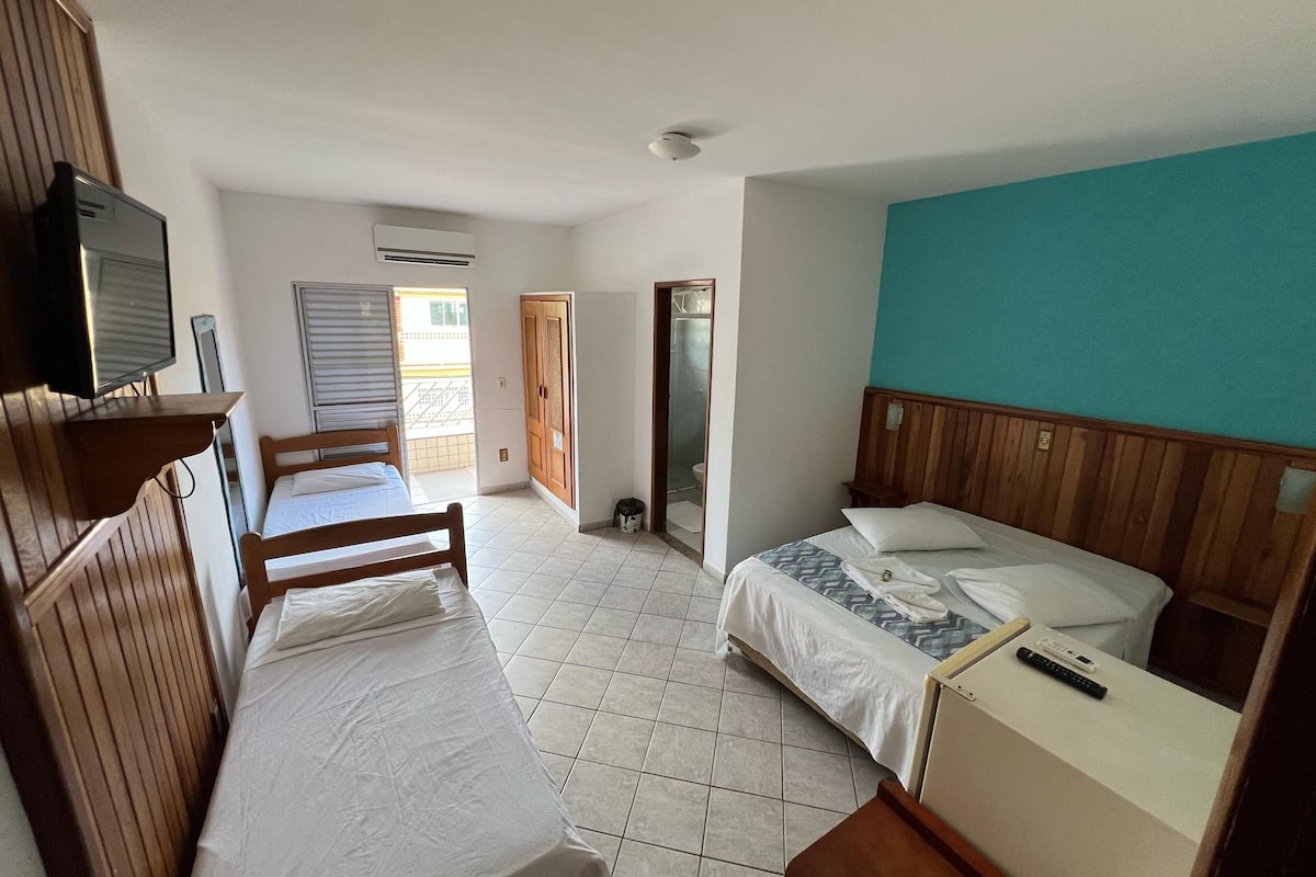 Quarto de hotel com duas camas, televisão, guarda-roupa e casa de banho visível através de uma porta aberta.