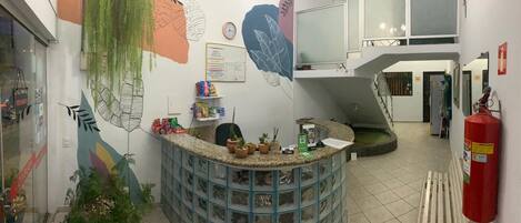 A reception area with a curved counter, potted plants, a fire extinguisher, and a staircase in the background.