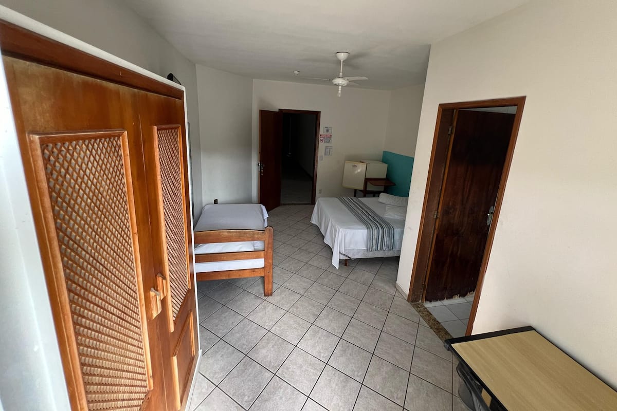 Quarto com cama, cadeira, escrivaninha e ventilador de teto.