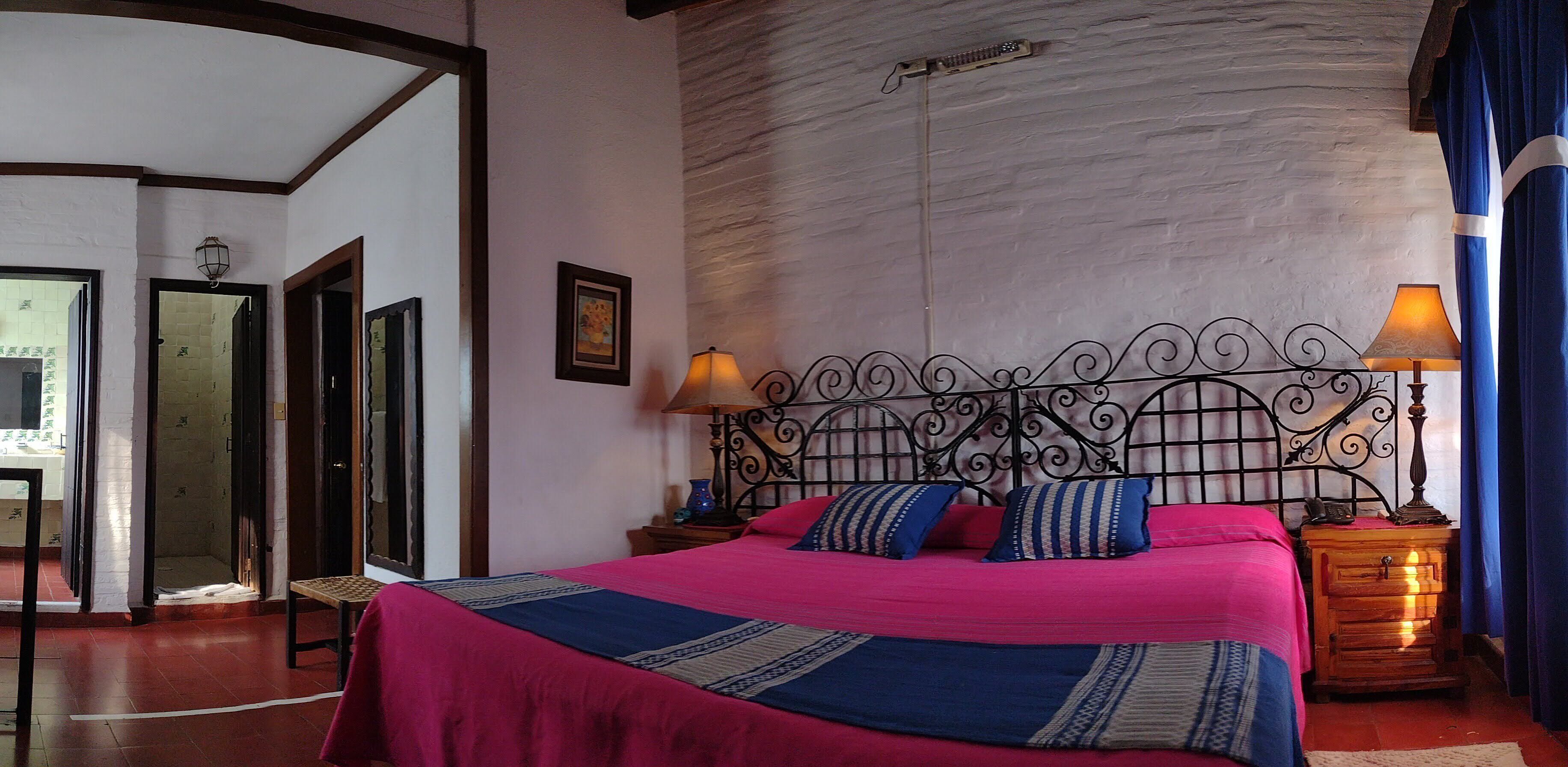 A bedroom with a metal headboard, two bedside lamps, a bed with pink and blue bedding, and a wooden nightstand.