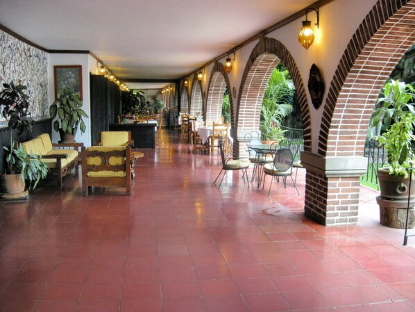 A spacious lobby with red tiled flooring, wooden furniture, and potted plants.