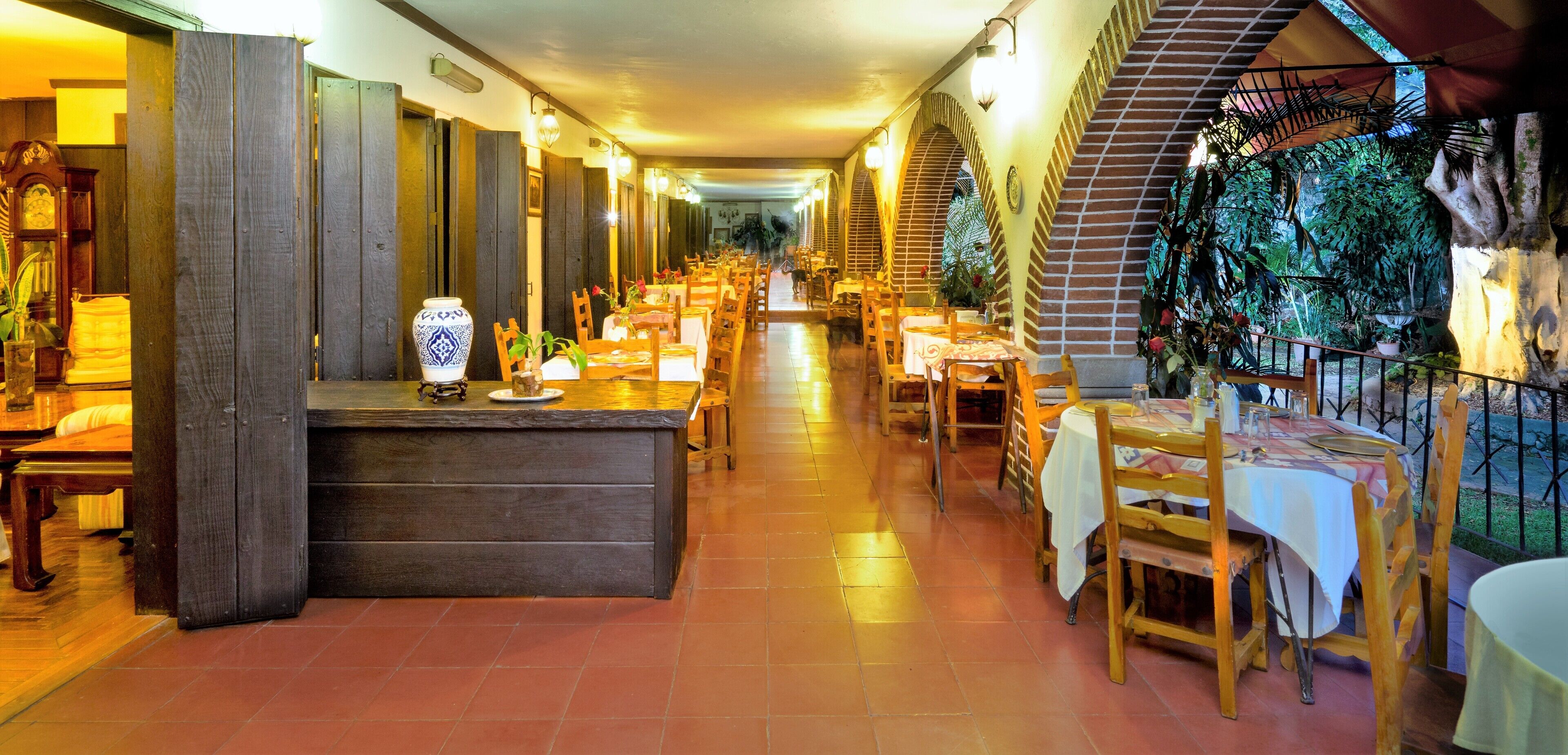 A restaurant with a long counter, wooden chairs, and tables with white tablecloths.