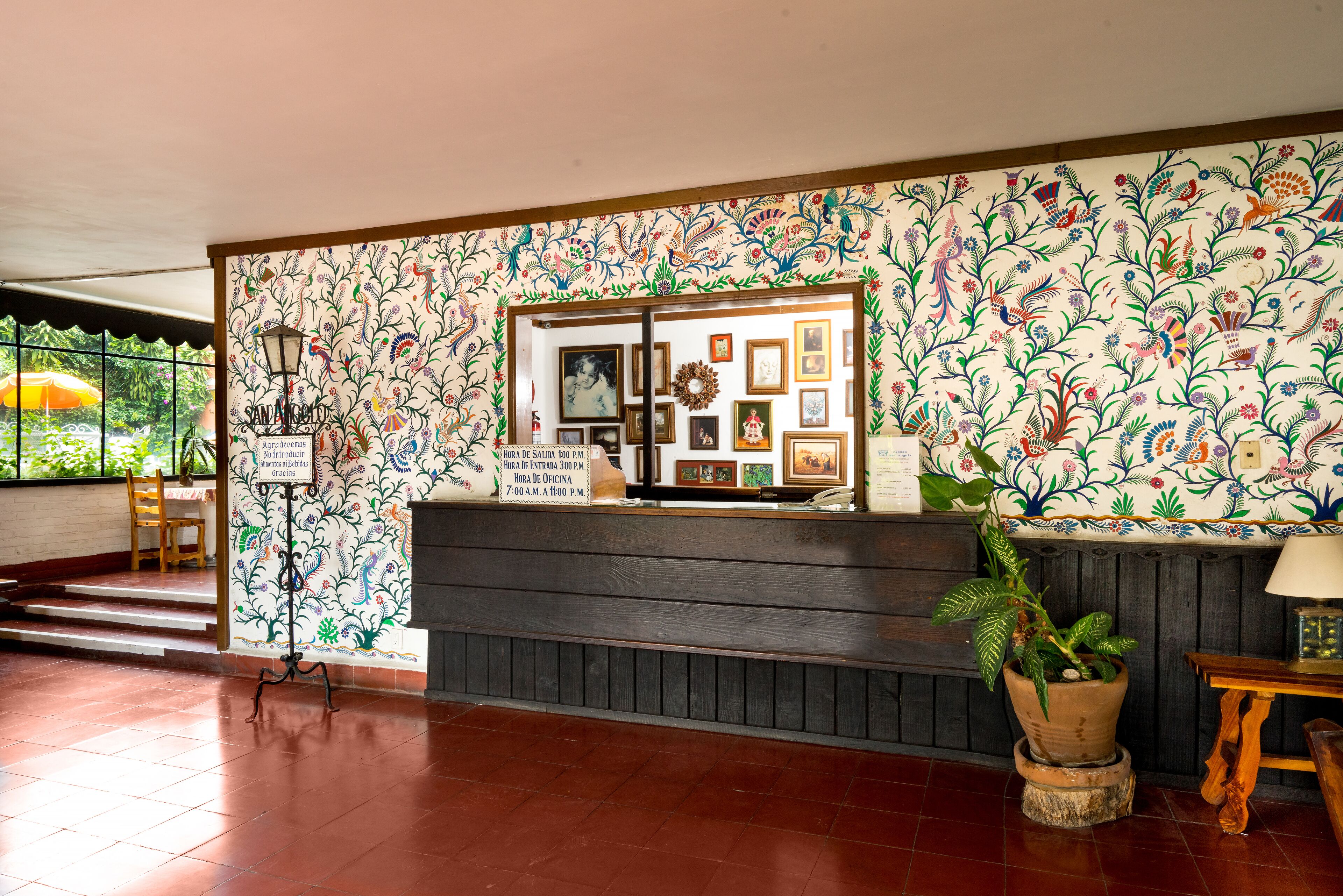 Zona de recepción con pared estampada con motivos florales, mostrador de madera y planta en maceta.