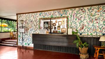 Zona de recepción con pared estampada con motivos florales, mostrador de madera y planta en maceta.