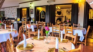 Un restaurant avec des tables et des chaises en bois, des nappes blanches et des assiettes à bord doré.