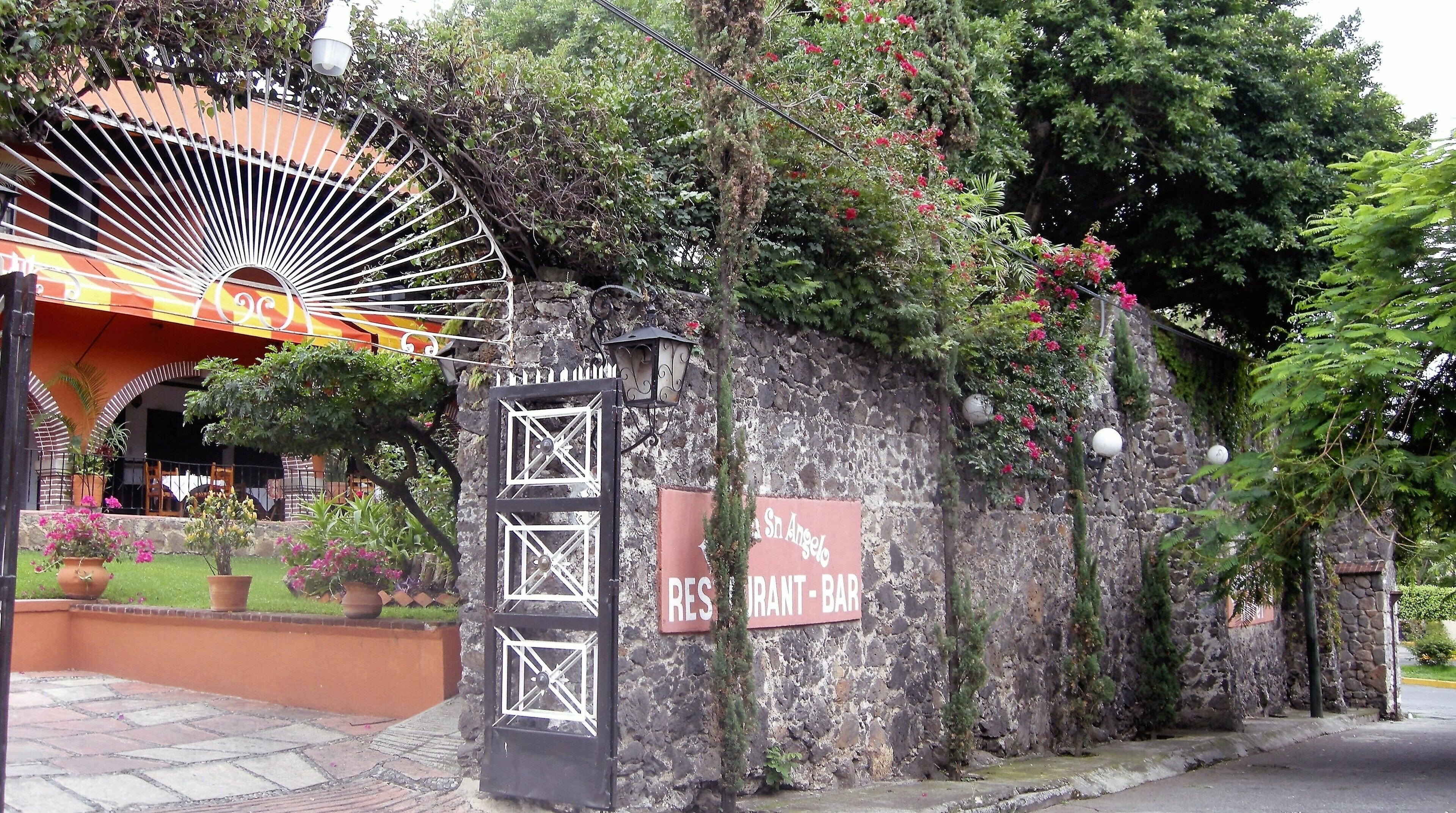 A stone wall with a restaurant-bar sign, a metal gate, and a colorful awning.