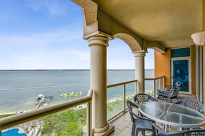 Un balcon avec une table et des chaises en verre, donnant sur une plage où se trouvent des bateaux et offrant une vue dégagée sur la mer.