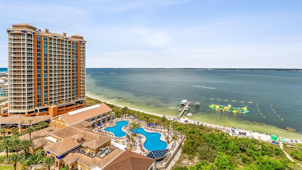 A high-rise hotel with multiple balconies overlooking a beach and a swimming pool area. - Summer is here @ Portofino 2-1409! (Pensacola Beach)