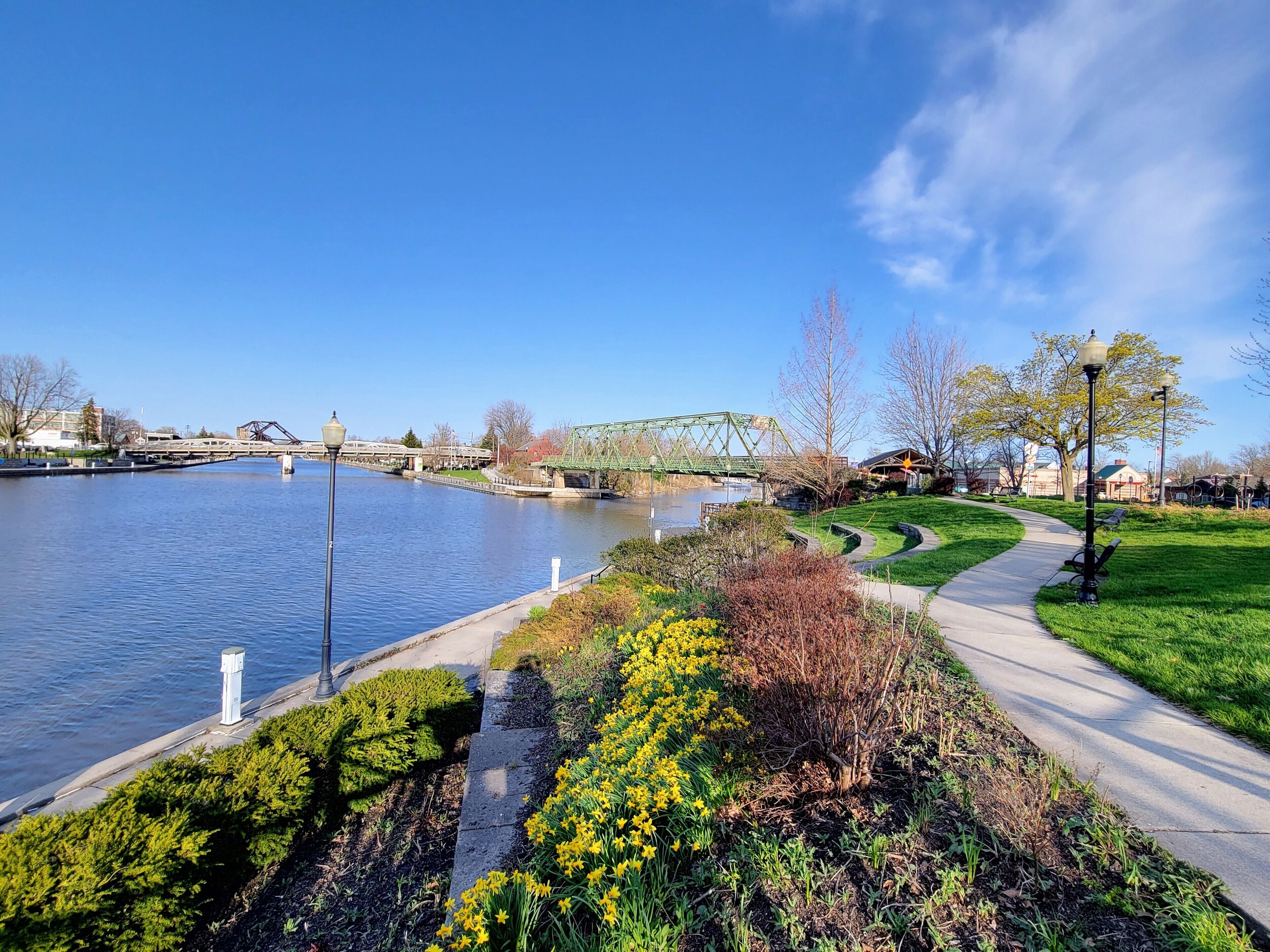 Une promenade au bord de la rivière, agrémentée d’un pont, d’espaces verts et de lampadaires.
