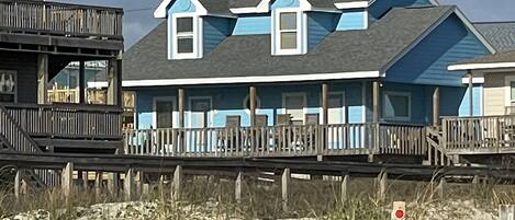 A beachfront house with a wooden deck and a balcony.