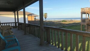 Una terraza de madera con barandilla que da a una playa, con sillas y un área cubierta al fondo.