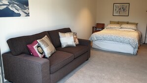 Ein Schlafzimmer mit einem braunen Sofa, einem Bett mit gemusterten Bettwaren, einem gerahmten Bild an der Wand und einer Stehlampe.