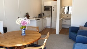 Eine moderne Küche mit weißen Geräten, ein Essbereich mit Holztisch und -stühlen sowie ein blaues Sofa im Wohnzimmer.