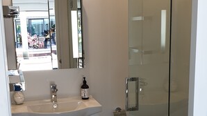 Ein modernes Badezimmer mit Duschkabine aus Glas, einem weißen Waschbecken mit Spiegel darüber und Holzboden.