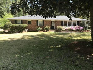 Traditional home with a central entrance, flanked by windows, set amidst a well-manicured lawn with flowering shrubs and trees.