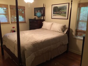 Relax in a serene bedroom with a four-poster bed, dresser, and globe, featuring a framed picture and a window with a view.