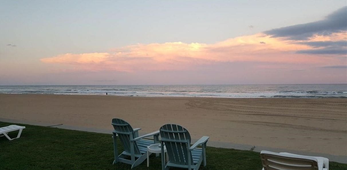 A beach view from a backyard with chairs and a table.