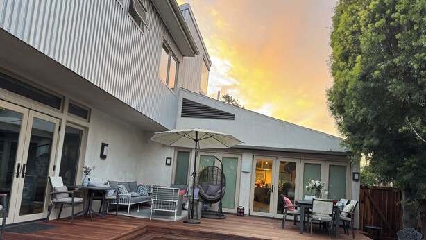 Un patio moderno con cubierta de madera, mobiliario exterior y un gran paraguas.