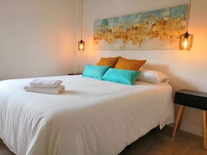 A neatly made bed with white linens and two pillows, a painting on the wall, and two hanging light fixtures. - The stop - 7.La PAN.123 (Zaragoza)