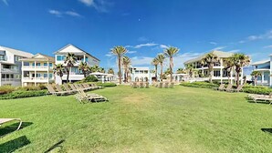A resort with multiple buildings, a grassy lawn, and palm trees.
