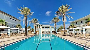 A swimming pool with lounge chairs and palm trees, surrounded by buildings with balconies.