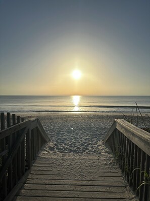 A wooden boardwalk leading to a beach with the sun setting in the distance. - Direct Oceanfront Paradise with Gigabit Internet and 55” 4K Streaming TV! (Palm Coast)