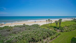 A coastal view with a beach, palm trees, and a golf course.