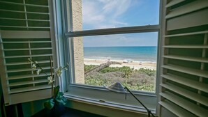 A room with a large window overlooking a beach, a potted plant, and a desk lamp.
