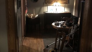 Un pasillo estrecho que conduce a una cocina con una mesa de comedor y sillas, una lámpara de araña y un cuadro en la pared.