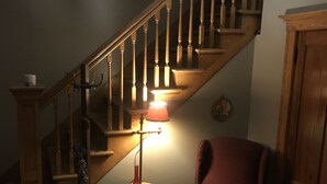 Una escalera con barandillas de madera, una silla roja, una lámpara y un adorno sobre una mesita.