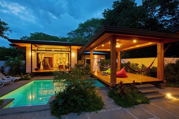 A modern house with a swimming pool, wooden deck, and a hammock.