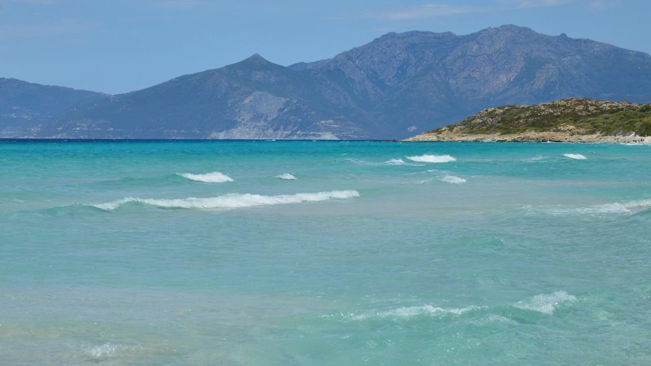 A coastal view with clear turquoise waters and distant mountains.