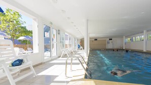 An indoor swimming pool with clear glass walls, white lounge chairs, and a lifeguard stand. - Appartement Cosy Equipée |  Accès Piscine (Le Tronchet)