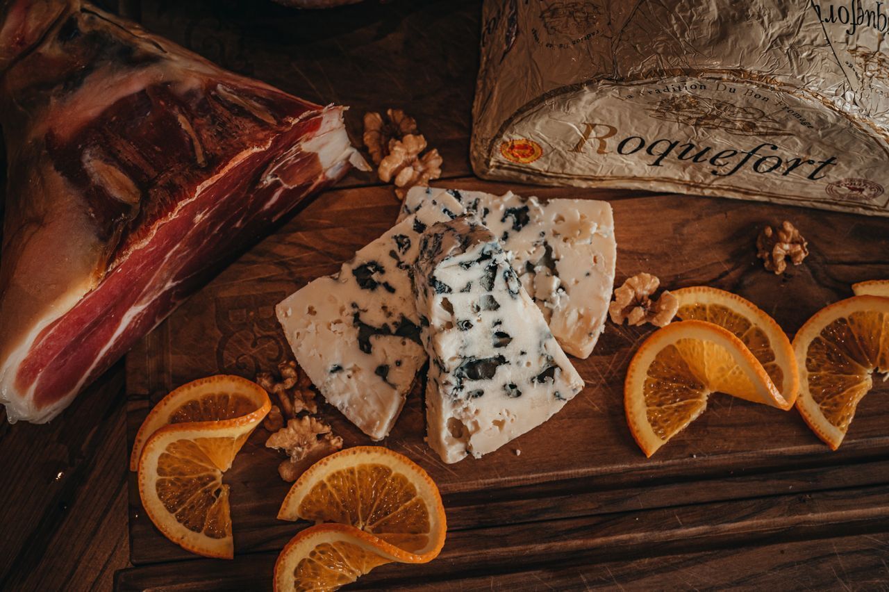 A wooden surface with a large piece of meat, cheese, walnuts, and orange slices.