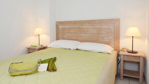 Een keurig opgemaakt bed met een groene sprei, twee nachtkastjes met lampen, een groene tas en een wit kussen op het bed.