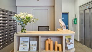 A reception desk with a sign reading "Odaly's" above it, a vase of flowers, and informational brochures on the counter. - Chambre Confortable et Abordable près du RER (Rueil Malmaison)