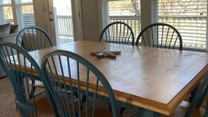 A dining area with a wooden table and six chairs, large windows with blinds, and a view of a deck. - Cozy 3br cottage on sound side near beach (Kill Devil Hills)