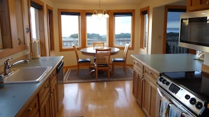 A kitchen with wooden cabinets, a stainless steel sink, a dining table with chairs, and a large window overlooking a scenic view.