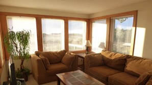 A living room with a brown sofa set, a coffee table, and a TV on a stand. There is a plant and a lamp on a side table.
