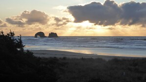 A beach with waves, a sunset, and two rock formations in the distance.