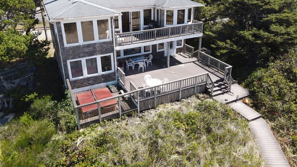 A two-story house with a balcony and a deck, surrounded by trees and hills.