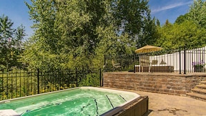 Ein Whirlpool, umgeben von einer Ziegelmauer und einem Metallzaun, mit Bäumen im Hintergrund.