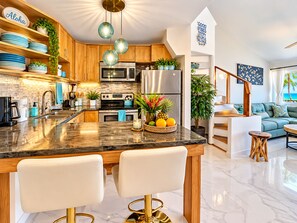 A modern kitchen with a marble countertop, stainless steel appliances, and a seating area with a view of the ocean. - Stunning Upstairs Unit with Direct Ocean View, Steps to  Beach.  Heart of Kihei (Kihei)