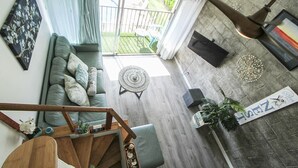 A spacious living area with a large window, a sofa with cushions, a round table, and a staircase leading to another level. - Full Ocean View! Prime Kihei Location!  (Kihei)