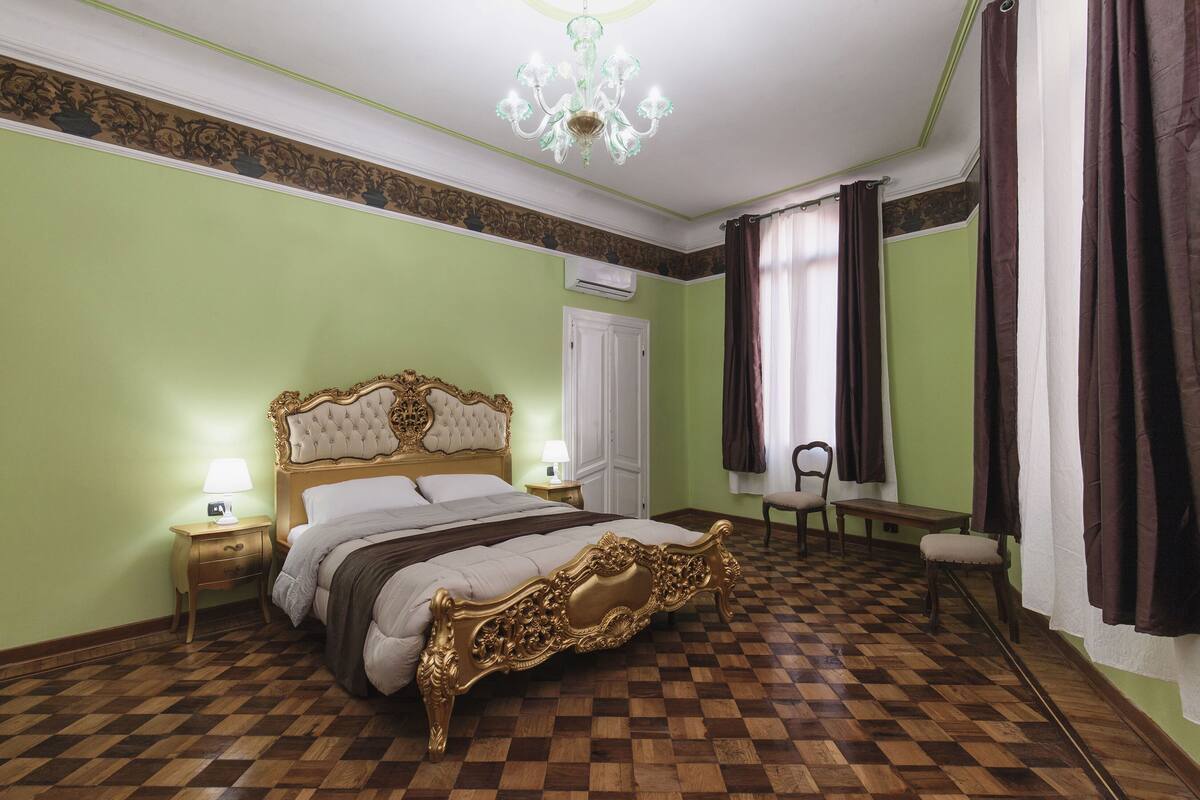 Une chambre avec un sol à carreaux, un grand lit à baldaquin décoré, un lustre et une chaise près de la fenêtre.