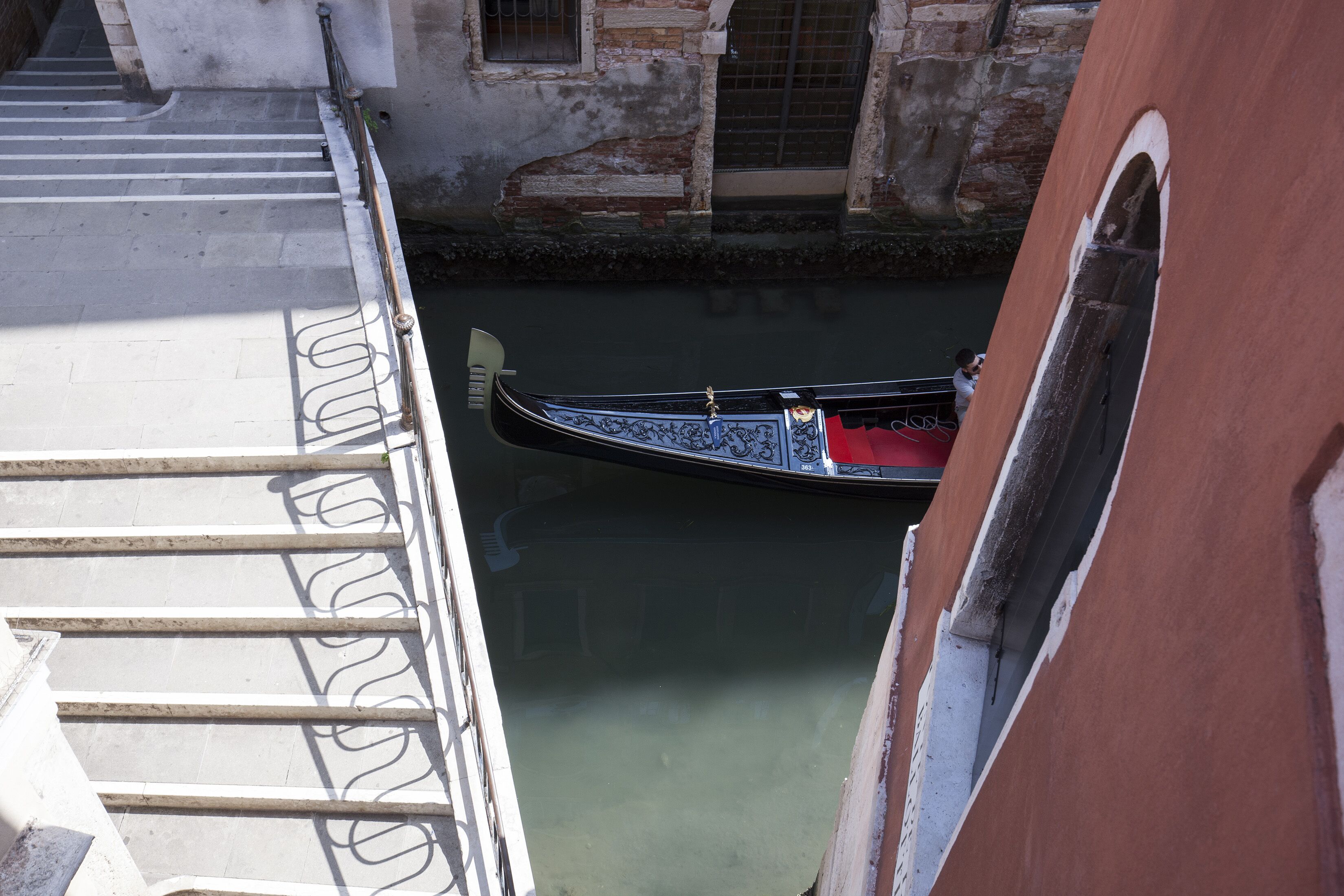 A gondola in a narrow canal, with a building and a staircase on one side.