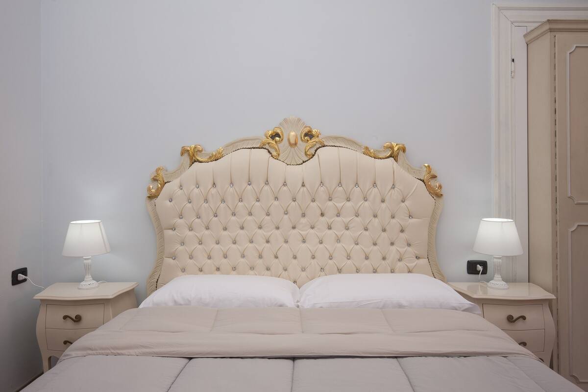 Un lit avec une tête de lit capitonnée, deux tables de chevet avec des lampes et une porte sur la droite.