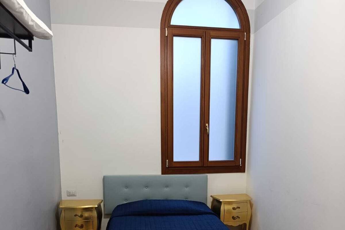 Une chambre à coucher comprenant un lit, deux tables de chevet, une fenêtre et un porte-vêtements suspendu.