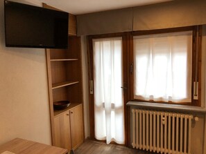 Una habitación con un armario de madera, un televisor de pantalla plana, una ventana con cortinas y un radiador.