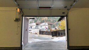 A garage entrance with a metal door, a telephone, and a view of a parking area with cars and a building in the background. - PETITE MAISON: 50 steps from the cable car !!! (Courmayeur)